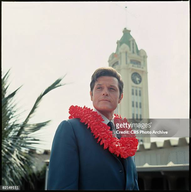 Low-angle view of American actor Jack Lord , , in character as Steve McGarrett, as he stands with a lei around his neck in a scene from the...