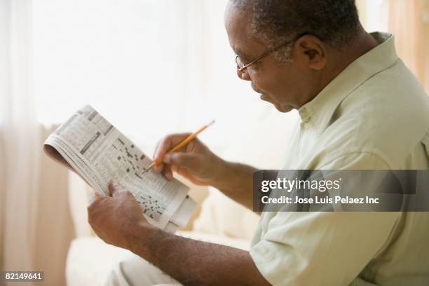 senior african man doing crossword puzzle - senior puzzle stock pictures, royalty-free photos & images