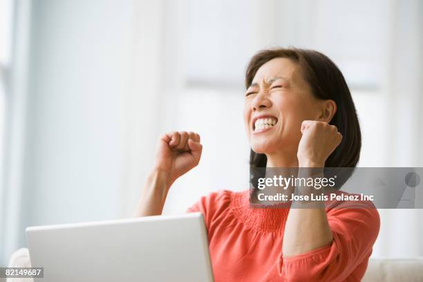 asian woman cheering next to laptop - business woman cheering stockfoto's en -beelden