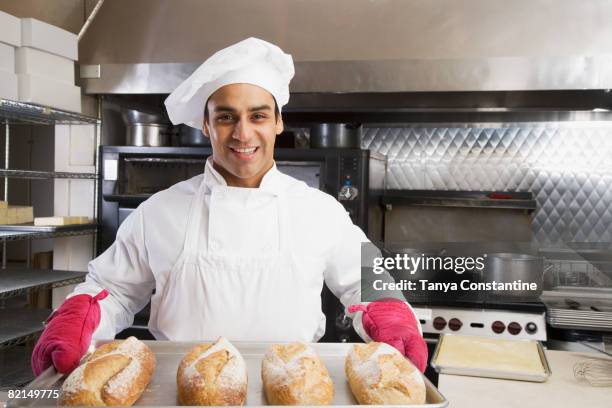 hispanic male baker holding tray of fresh bread - kochmütze stock-fotos und bilder