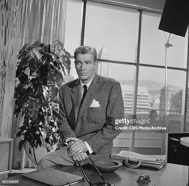 American actor William Hopper , as character Paul Drake, sits on the edge of a desk on the set of 'Perry Mason' entitiled 'The Case of the Moth-Eaten...