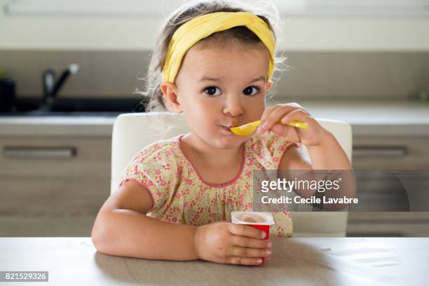 toddler girl eating yogurt - peuter stockfoto's en -beelden