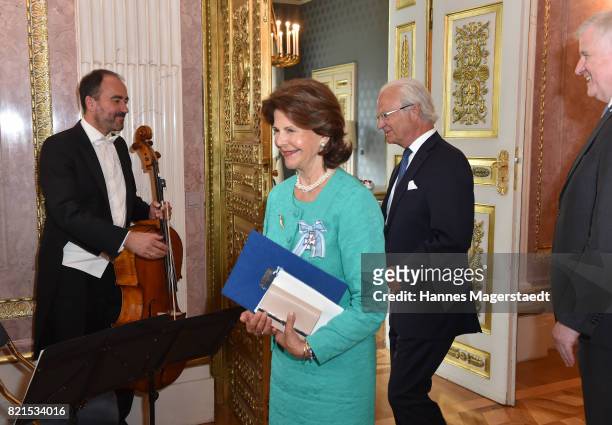 Queen Silvia of Sweden stands next to her husband King Carl XVI Gustaf of Sweden as she is awarded the Bavarian Order of Merit at Prinz-Carl-Palais...