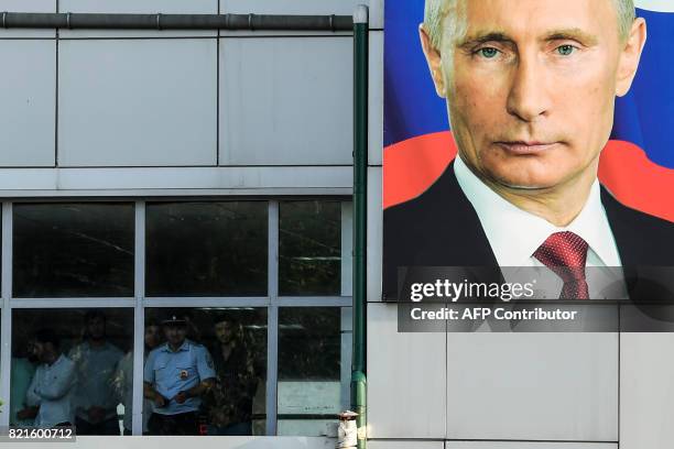 People look out of a window at Grozny Airport adorned with a portrait of Russian President Vladimir Putin in Grozny, on July 24, 2017. / AFP PHOTO /...