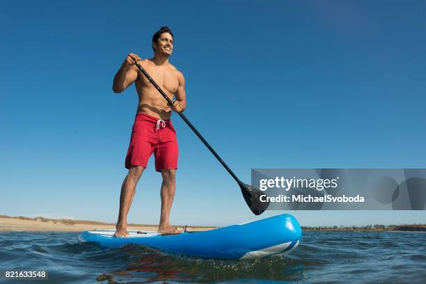 man stand up paddle boarding - muscle men at beach stockfoto's en -beelden