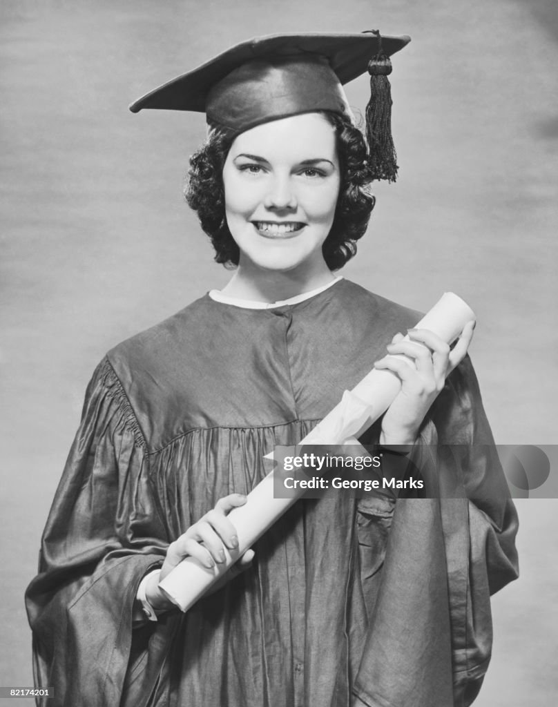 Woman wearing graduation gown holding diploma, (B&W), portrait