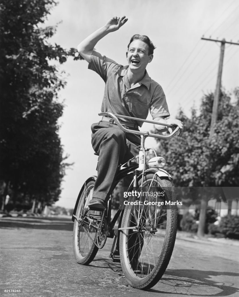 Man riding bicycle, waving, (B&W)