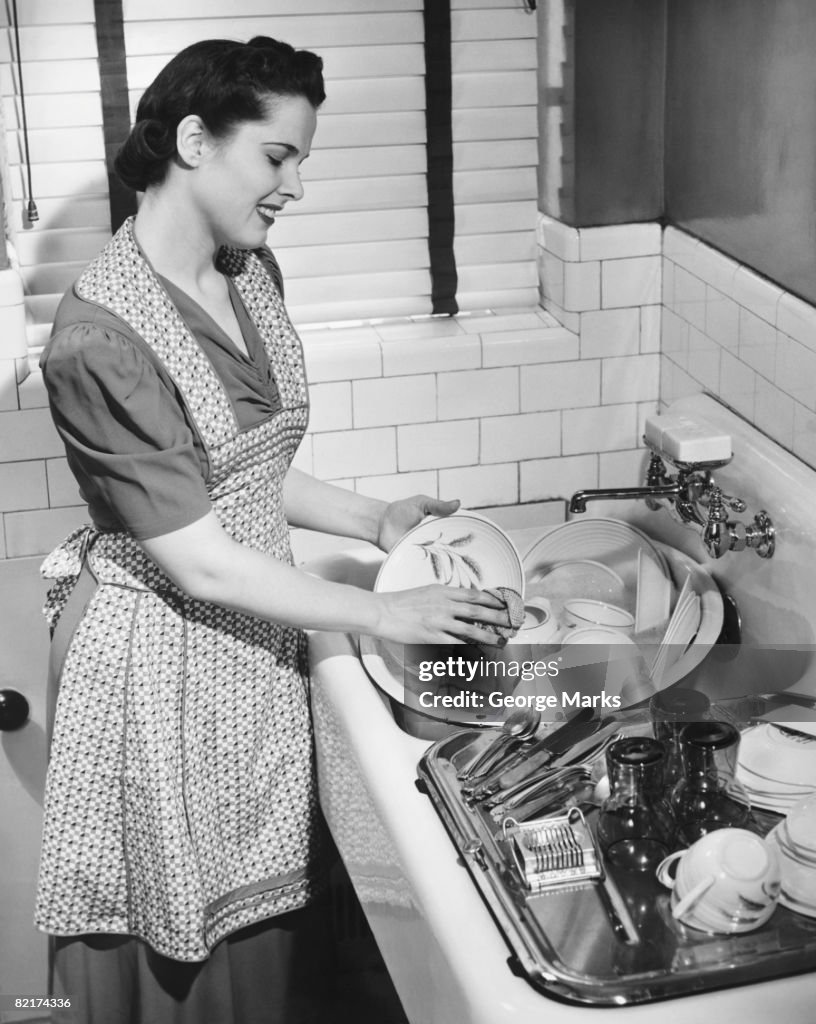 Woman washing dishes in kitchen sink, (B&W)