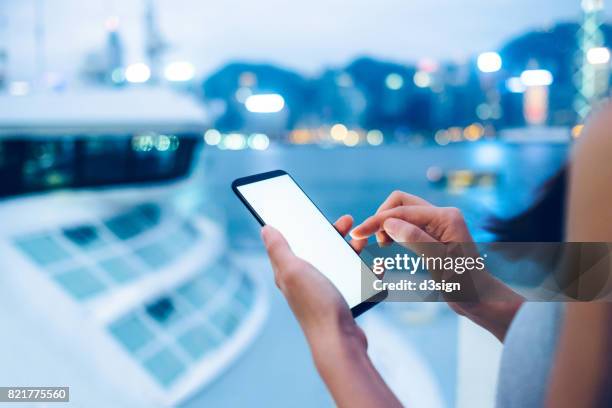 woman using smartphone next to a cruise by the victoria harbour at sunset - luxury city break stock pictures, royalty-free photos & images