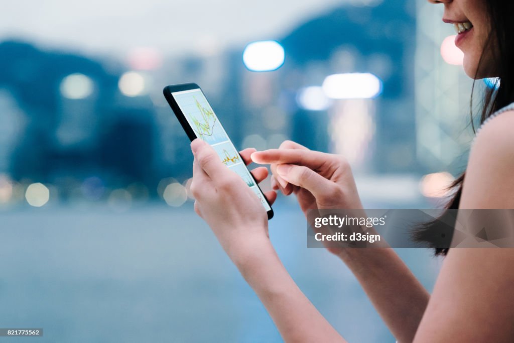 Woman checking financial trading data with smartphone in city