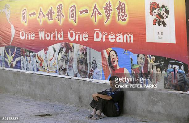 An ethnic Uighur sits under a poster of the 2008 Beijing Olympic Games on a street in Xinjiang's famed Silk Road city of Kashgar in China's far...