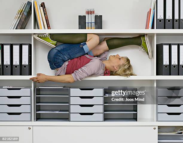 young woman stretching in office shelves - piernas en el aire fotografías e imágenes de stock