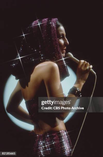 Rerouched promotional portrait of American singer and actress Cher as she sings while dressed in a two-piece sequinned costume for the television...