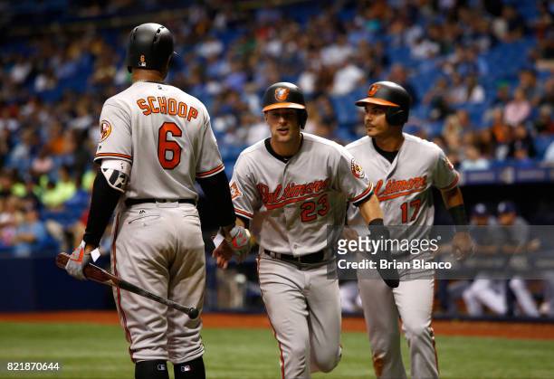 Joey Rickard of the Baltimore Orioles and Ruben Tejada celebrate with Jonathan Schoop as they make their way to the dugout after scoring off of a...
