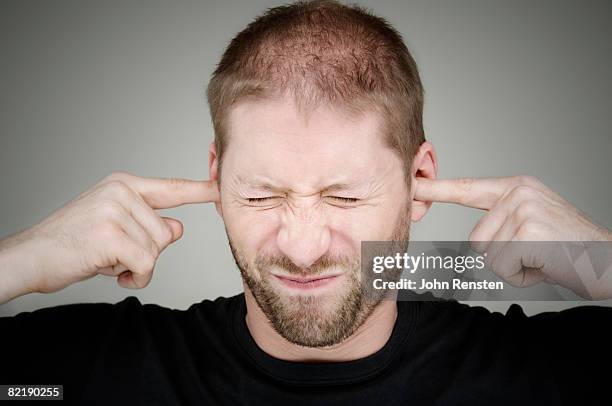 man with fingers in ears - hear no evil stock pictures, royalty-free photos & images