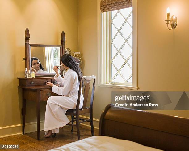 young woman applying make-up in front of a mirror - vanity stock pictures, royalty-free photos & images