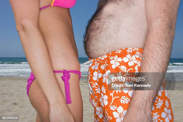 skinny woman and overweight man on the beach - pot belly fotografías e imágenes de stock