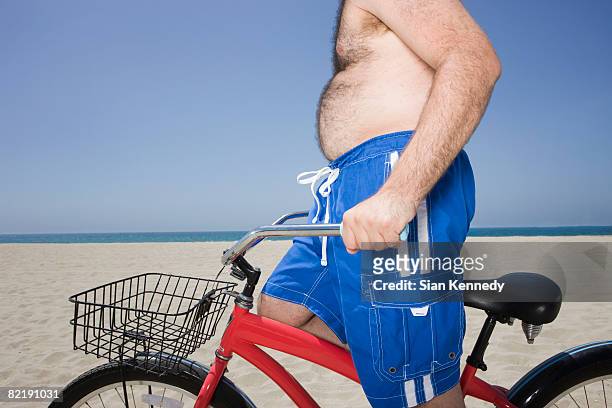 overweight man riding bike on the beach - fat guy on beach fotografías e imágenes de stock