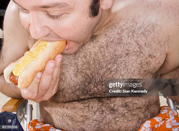 shirtless overweight man eating a hot dog - matière grasse aliment photos et images de collection