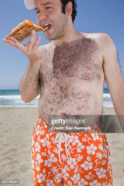 overweight man eating pizza on the beach - pens stockfoto's en -beelden