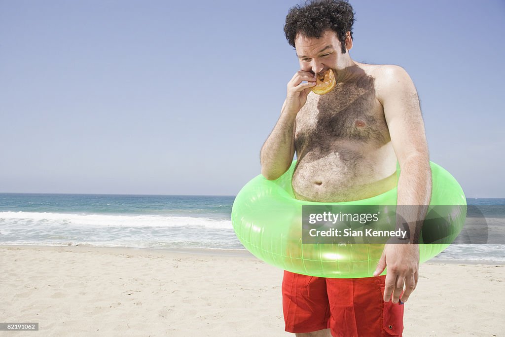 Man with pot belly eating a hamburger on the beach