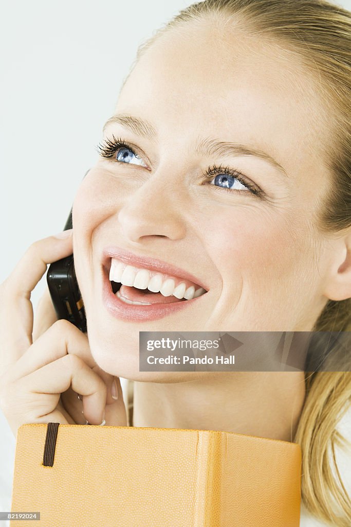 Woman using telephone, holding book, laughing