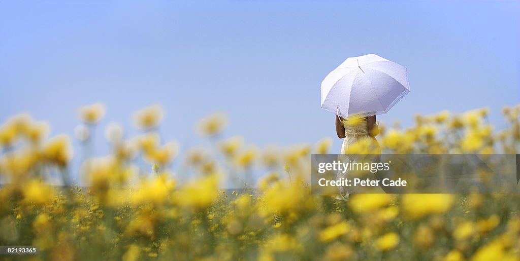 Woman holding umbrella in field of yellow flowers