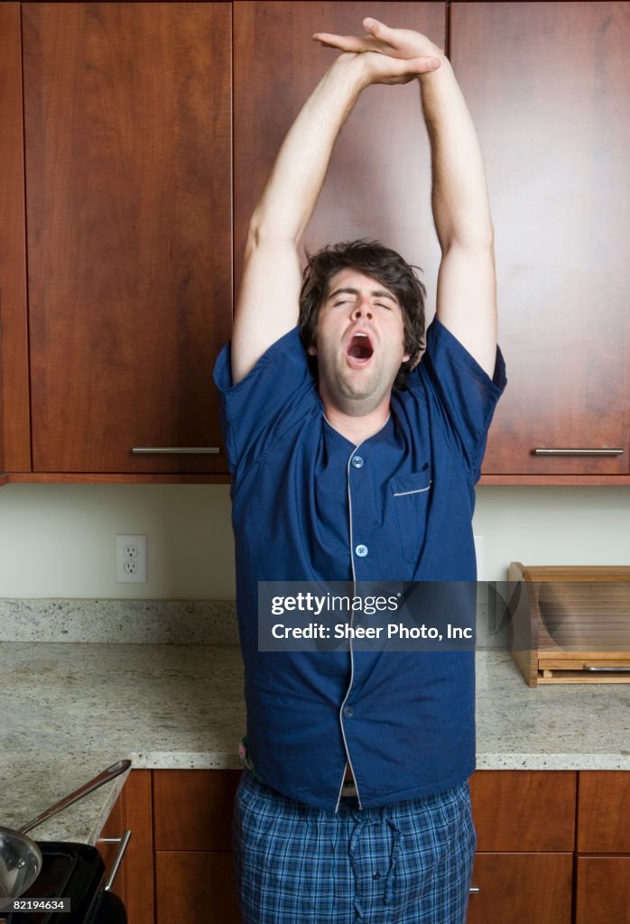 Man yawning and stretching in kitchen 