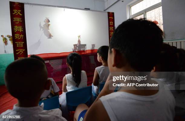 This photo taken on July 24, 2017 shows a group of volunteers from a shadow art troupe teaching "left-behind" children how to operate shadow puppets...