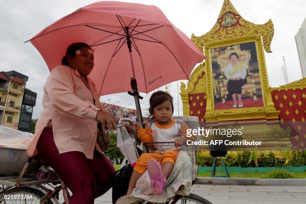 Cambodian food vendor pedals her bicycle with her daughter riding up front in Phnom Penh on July 25, 2017. / AFP PHOTO / TANG CHHIN SOTHY