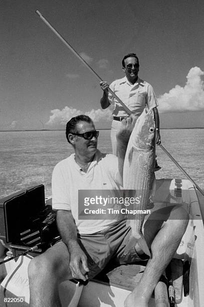 Baseball great Ted Williams, holds up a bonefish in the Bahamas while George Hommel poles the boat.