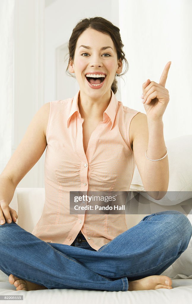 Young woman on couch pointing, laughing