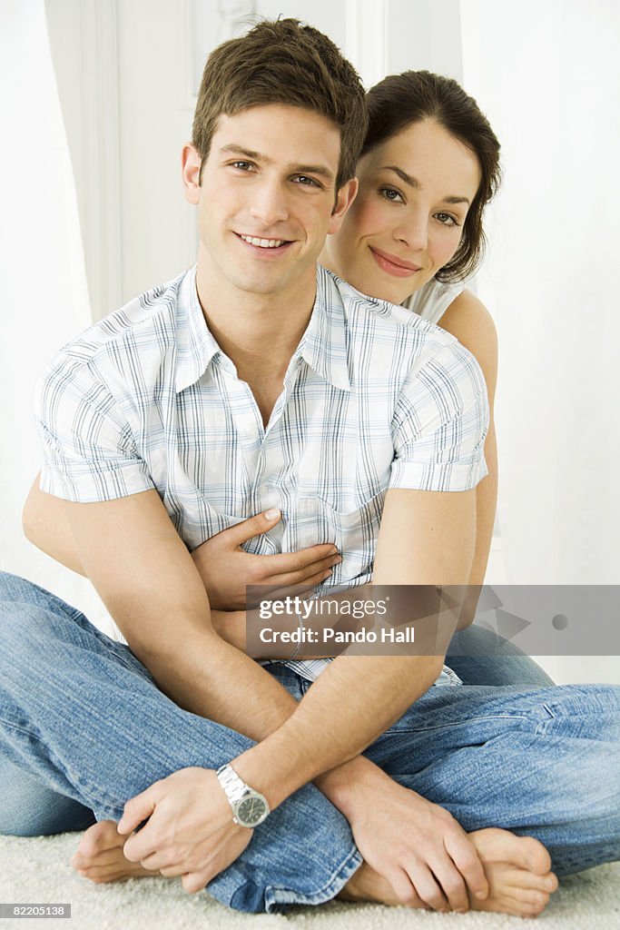 Young couple hugging, sitting on carpet, smiling