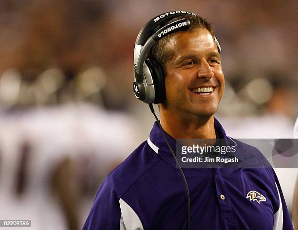 Coach John Harbaugh of the Baltimore Ravens smiles after a touchdown against the New England Patriots during a preseason game at Gillette Stadium on...
