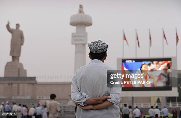 An ethnic Uighur watches the opening ceremony of the Olympic Games on a big screen in the main square in Xinjiang's famed Silk Road city of Kashgar...