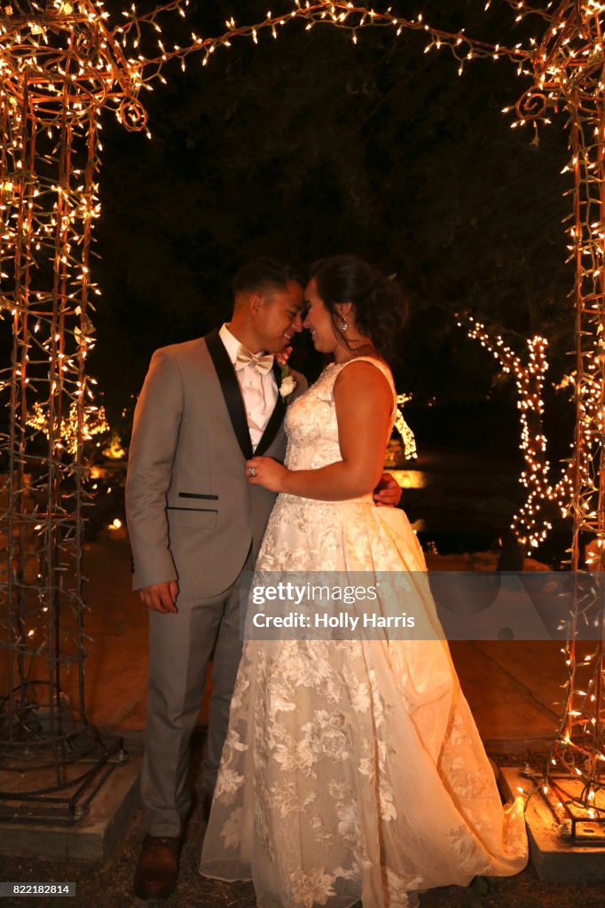 Bride and groom touching noses under illuminated arch at night