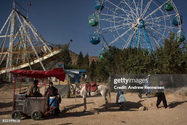 Horse stands in front of amusement park rides at Qargha Lake, a popular weekend destination on the outskirts of Kabul, on July 21, 2017 in Kabul,...