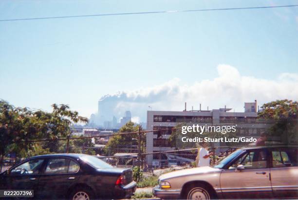 During the terrorist attacks of September 11 two people walk past a fence and parked cars as smoke is seen rising from the site of the World Trade...