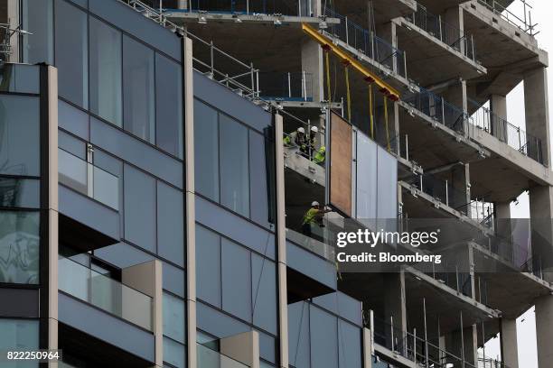 Workers move pieces of glass as they build residential flats on the Greenwich Peninsula construction site in London, U.K., on Tuesday, July 25, 2017....