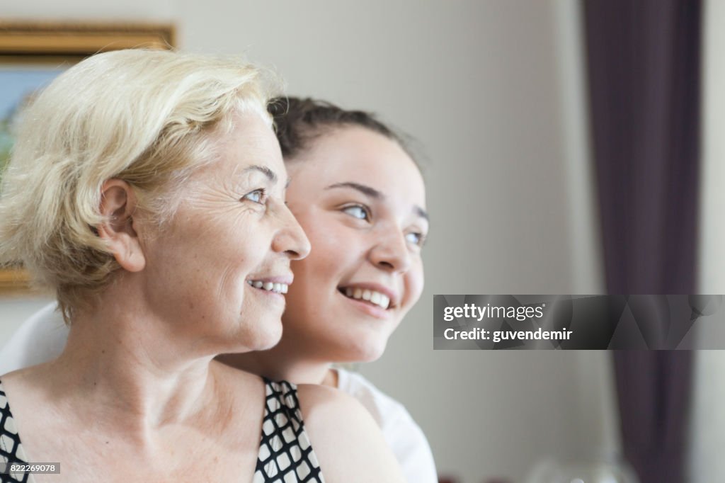 Smiling young daughter embracing her mother behind