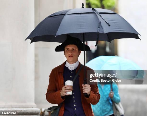 Joe Juknievich keeps his 18th century late Colonial costume dry in the rain on School Street near Downtown Crossing in Boston on Jul. 24, 2017. The...