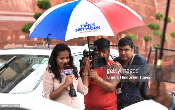 Crew members stand under an umbrella as they report in the heavy down pour after swearing-in ceremony of President Ram Nath Kovind at Parliament on...