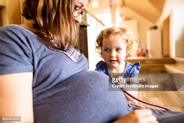 little girl with stethoscope on belly of her pregnant mother. - little kids belly imagens e fotografias de stock