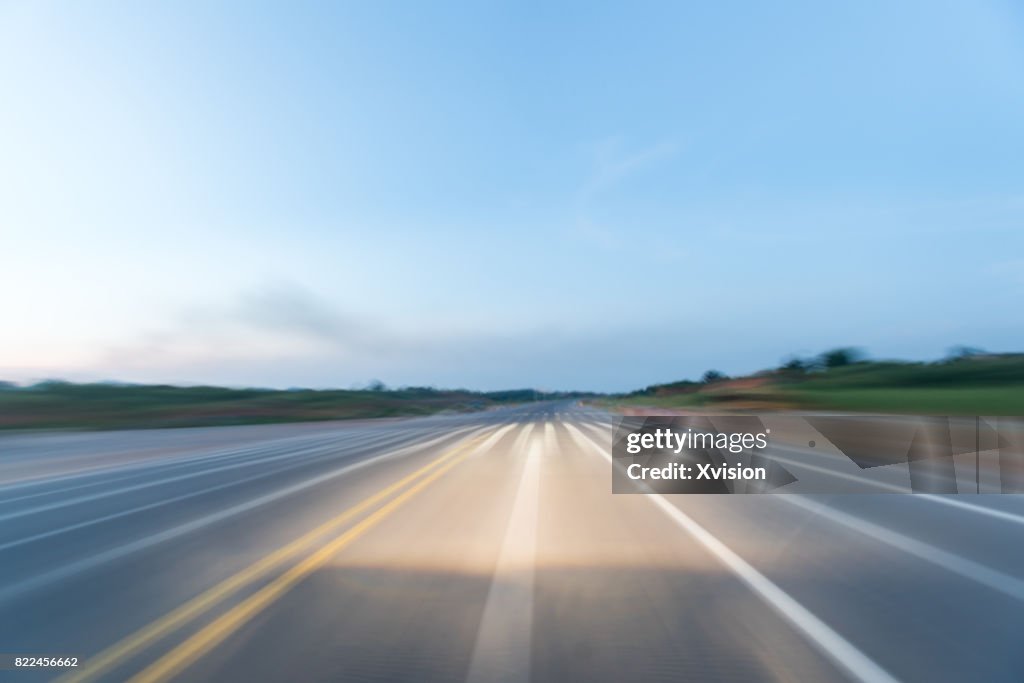 Asphalt road under blue sky with clouds in motion blur with plants in sides