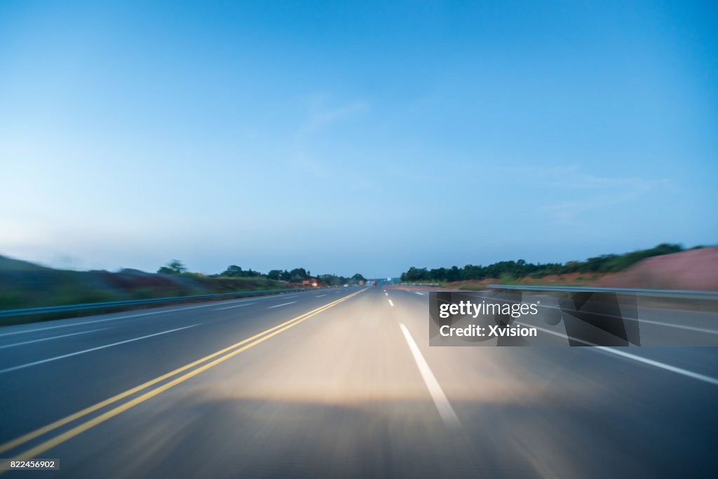Asphalt road under blue sky with clouds in motion blur with plants in sides