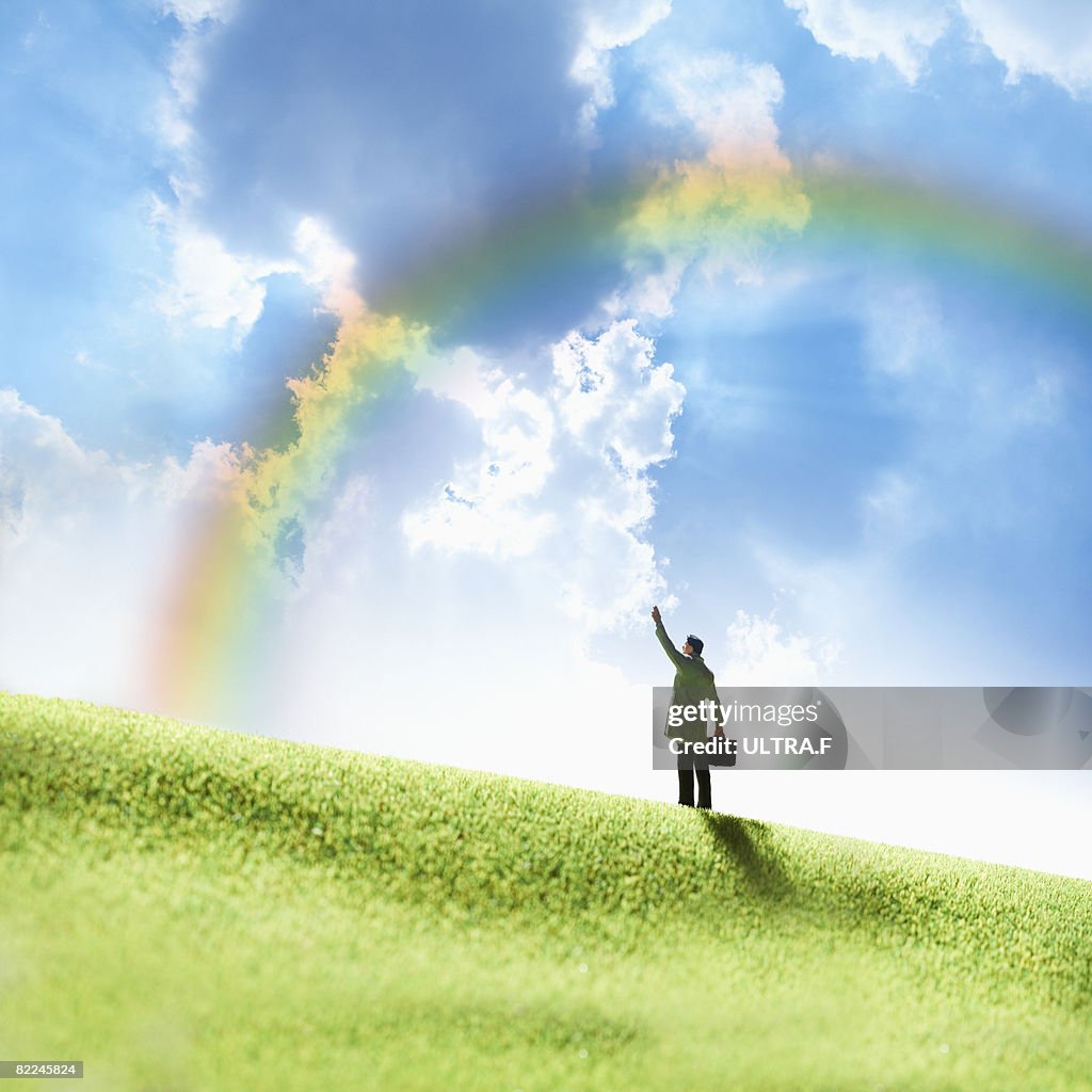 A man is waving his hand under a rainbow. 