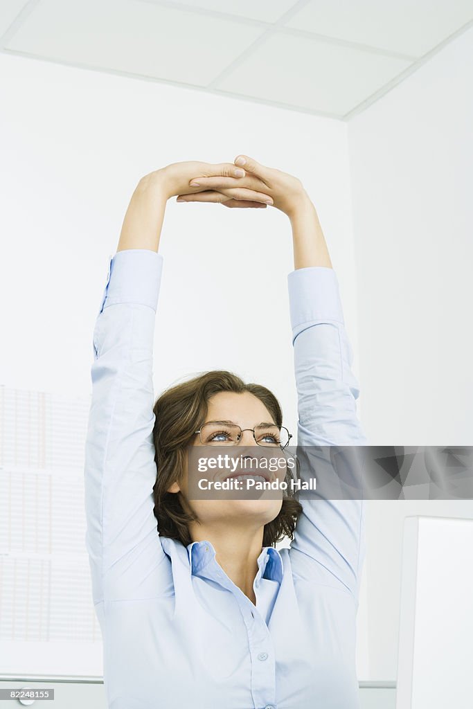 Woman in office, stretching arms, smiling