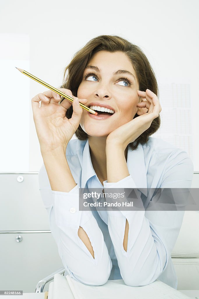 Woman sitting at desk with pencil in mouth