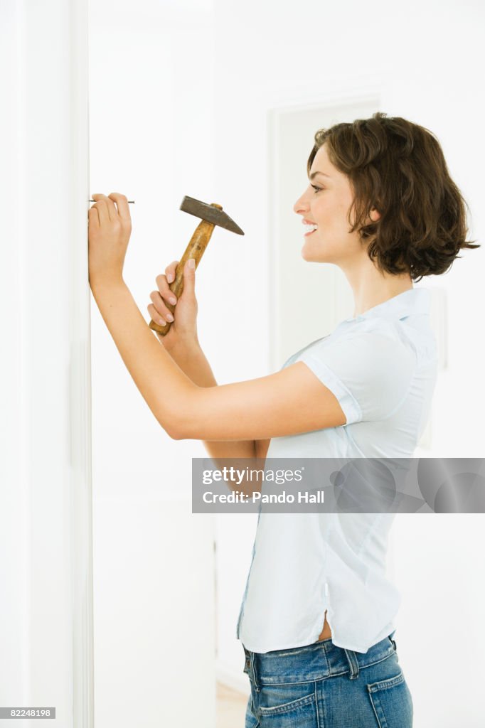 Woman hammering nail into wall, smiling