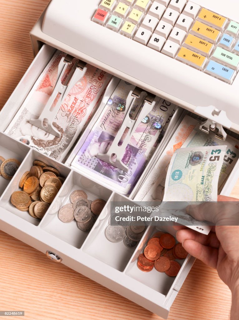 Cashier putting pounds sterling in cash register